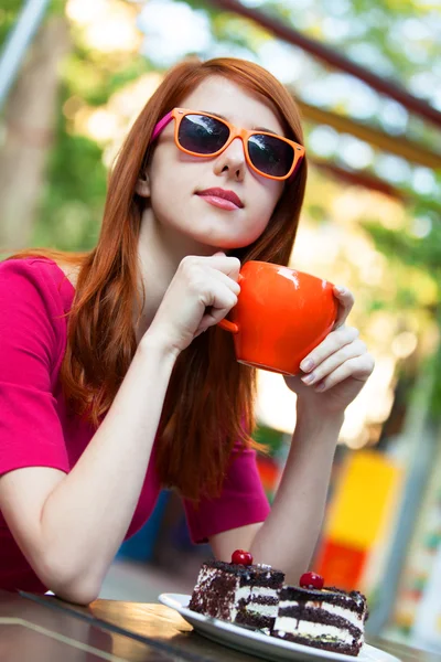 Stile rossa ragazza con tazza e torta seduta sulla panchina in — Foto Stock