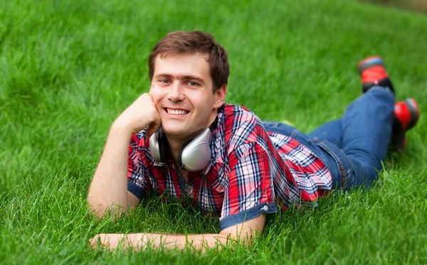 Beau jeune homme avec écouteurs à l'herbe verte — Photo