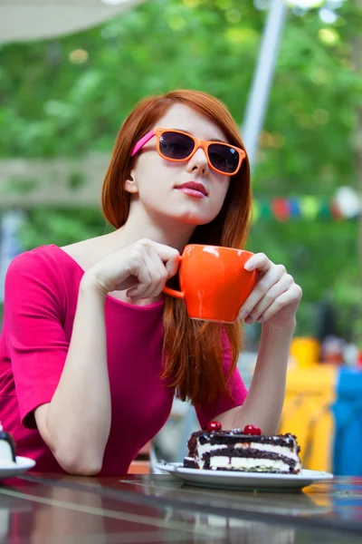 Stijl roodharige meisje met cup en taart zittend op de Bank in de — Stockfoto