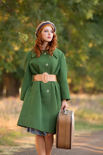 Rödhårig tjej med resväska på trädets alley. — Stockfoto