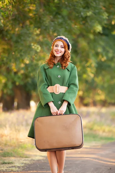 Redhead girl with suitcase at tree's alley. — Stock Photo, Image