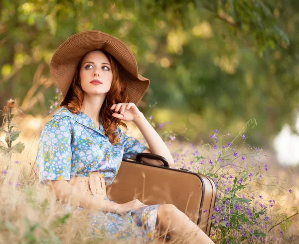 Pelirroja con maleta sentada en la hierba de otoño — Foto de Stock