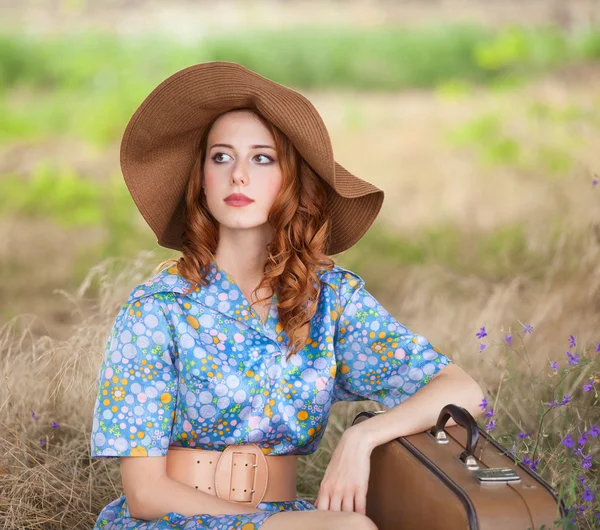 Roodharige meisje met koffer zittend op herfst gras — Stockfoto