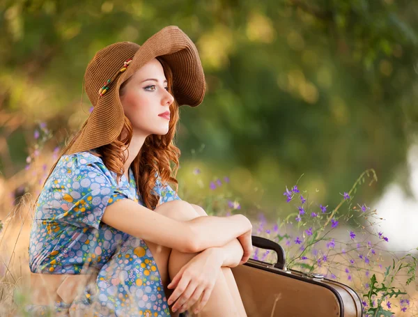 Roodharige meisje met koffer zittend op herfst gras — Stockfoto