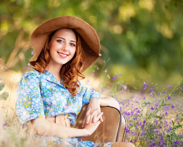 Roodharige meisje met koffer zittend op herfst gras — Stockfoto