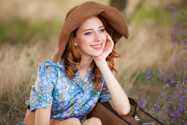 Roodharige meisje met koffer zittend op herfst gras — Stockfoto