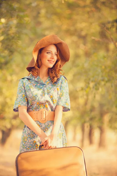 Redhead girl with suitcase at tree's alley. — Stock Photo, Image