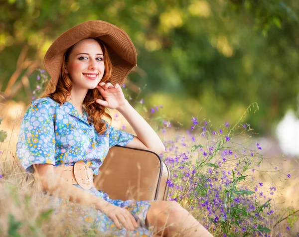 Pelirroja con maleta sentada en la hierba de otoño — Foto de Stock