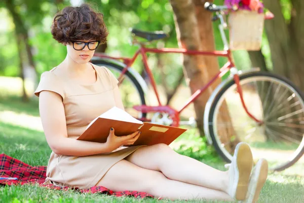 Brunette girl with note in the park. Retro bike at background. — Stock Photo, Image