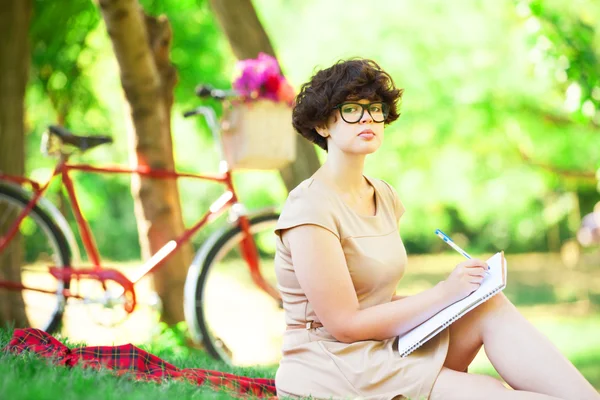 Menina morena com nota no parque. Bicicleta retro no fundo . — Fotografia de Stock