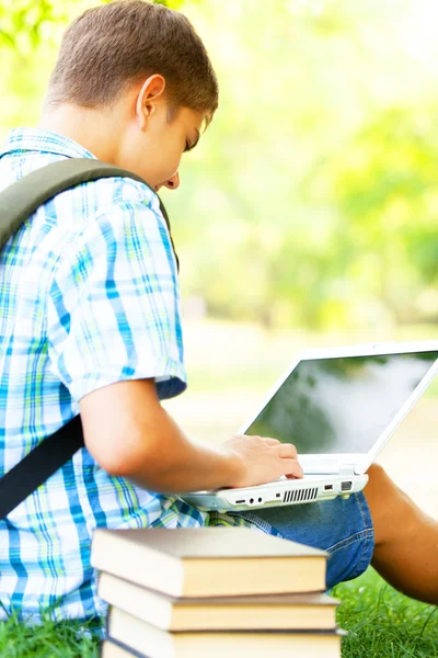 Adolescent garçon avec livres et ordinateur portable dans l 'parc . — Photo