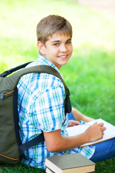 Tiener jongen met boeken en laptop buiten. — Stockfoto