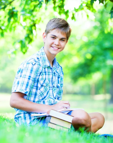 Tiener jongen met boeken en notebook in het park. — Stockfoto