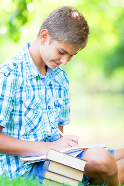 Tiener jongen met boeken en notebook in het park. — Stockfoto