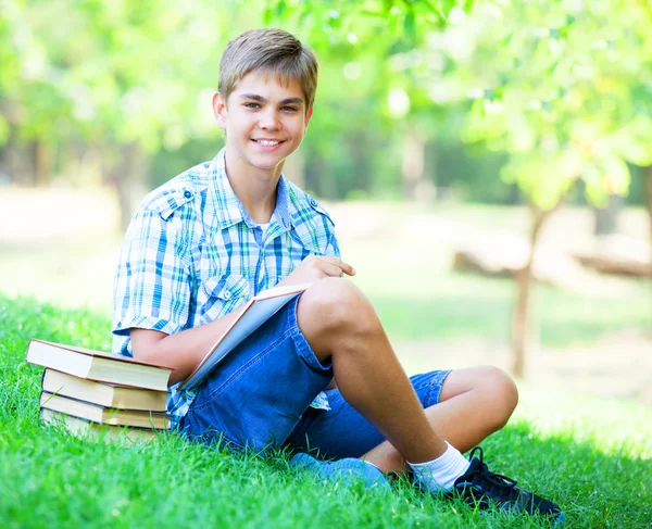 Tiener jongen met boeken en notebook in het park. — Stockfoto