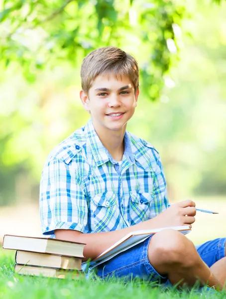 Tiener jongen met boeken en notebook in het park. — Stockfoto