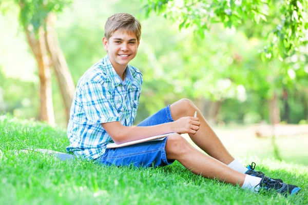 Tiener jongen met boeken en notebook in het park. — Stockfoto