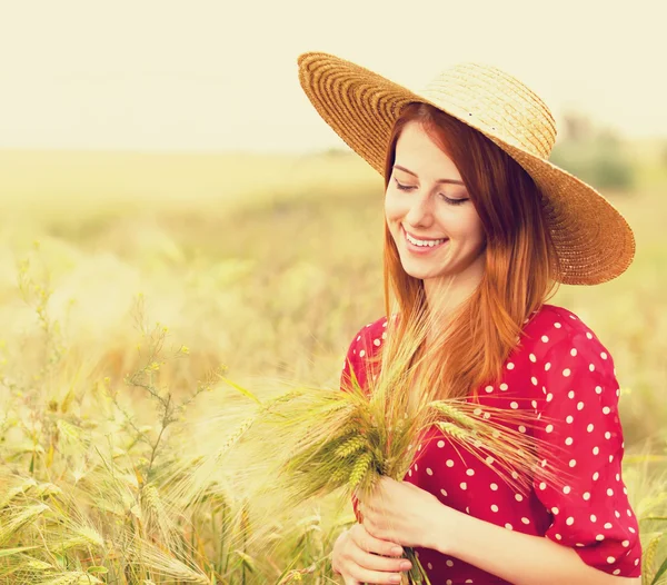 Roodharige meisje in een rode jurk aan het tarweveld — Stockfoto