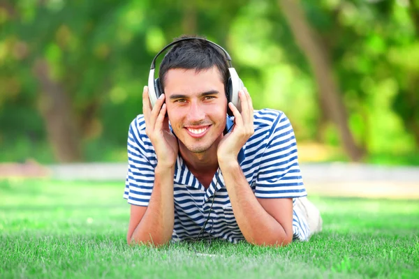 Jovem bonito com fones de ouvido na grama verde — Fotografia de Stock