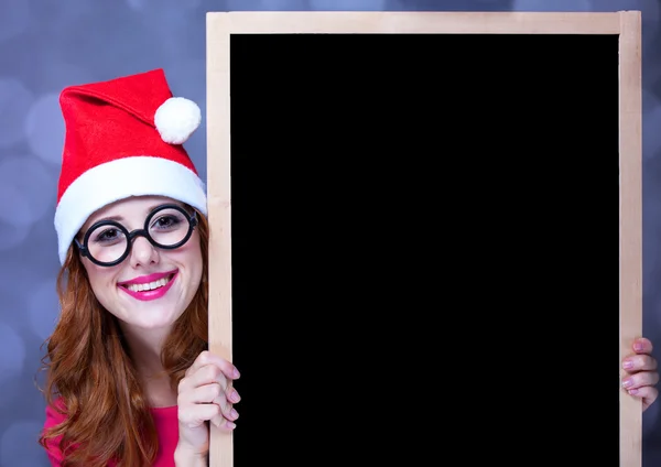 Rothaarige Mädchen mit Weihnachtsmütze und Tafel — Stockfoto