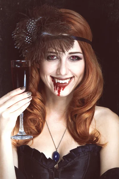 Redhead vampier vrouw met glas van bloed. foto in vintage styl — Stockfoto