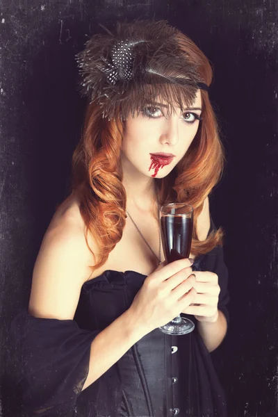 Mujer vampiro pelirroja con vaso de sangre. Foto en estilo vintage —  Fotos de Stock