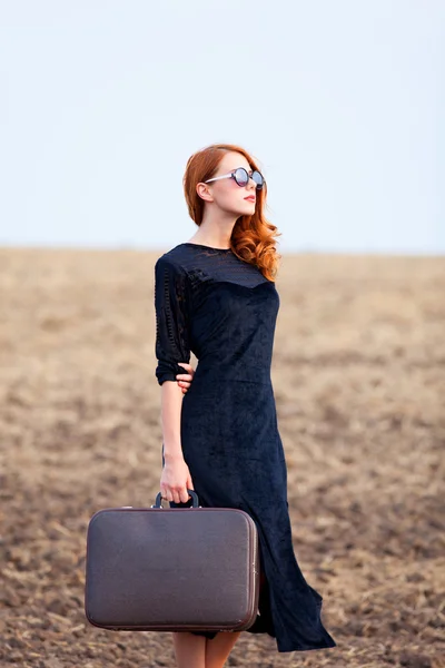 Redhead girl with suitcase at autumn field — Stock Photo, Image