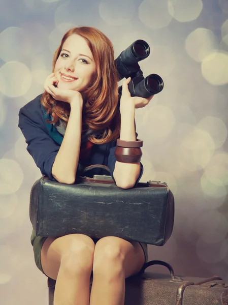 Roodharige meisje met verrekijker zittend op de grote koffer — Stockfoto