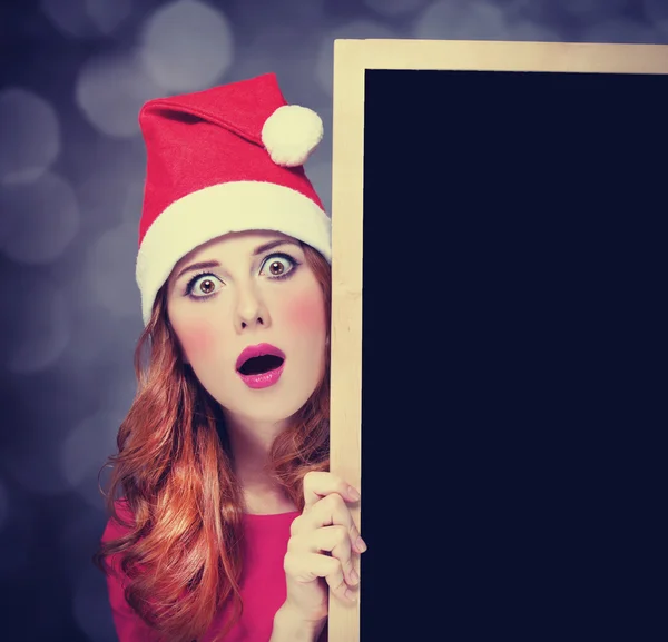 Menina ruiva em chapéu de Natal com quadro negro — Fotografia de Stock