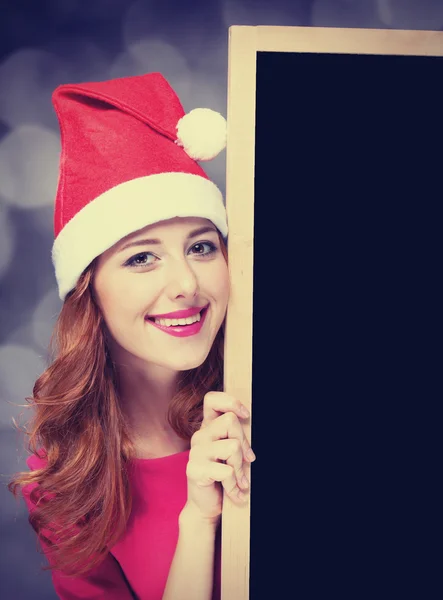 Κοκκινομάλλα κοπέλα με καπέλο Χριστούγεννα με μαυροπίνακα — Φωτογραφία Αρχείου
