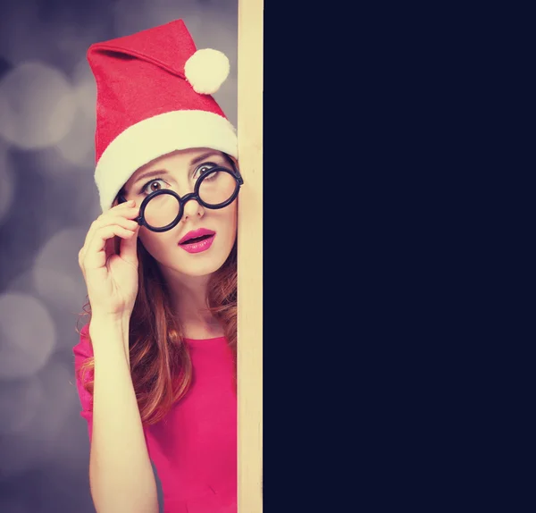 Menina ruiva em chapéu de Natal com quadro negro — Fotografia de Stock