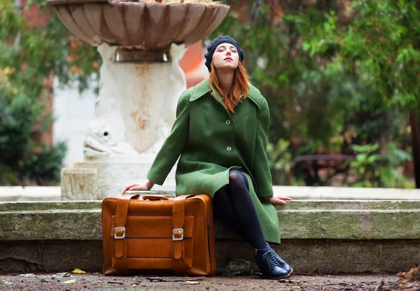 Pelirroja con maleta sentada en otoño al aire libre . — Foto de Stock