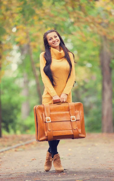 Ragazza bruna che tiene la valigia nel vicolo d'autunno nel parco — Foto Stock