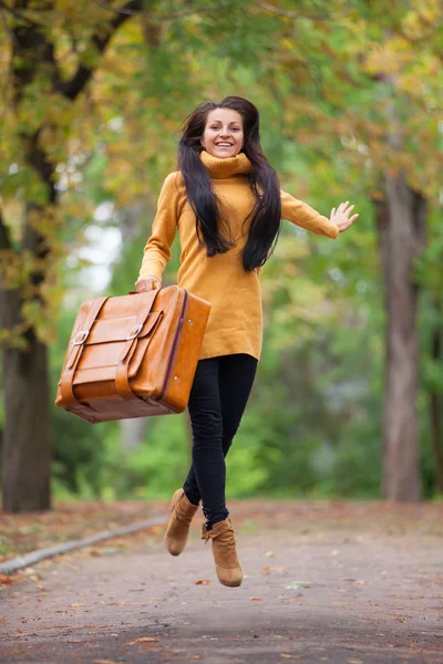 Chica morena sosteniendo maleta en el callejón de otoño en el parque — Foto de Stock