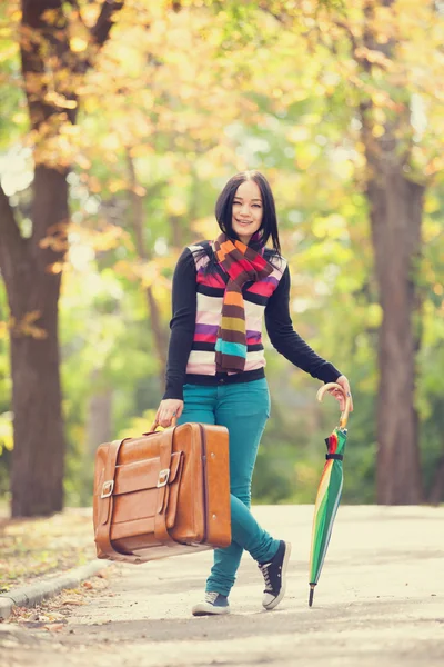 Bruna ragazza che tiene valigia e ombrello nel vicolo autunnale in t — Foto Stock