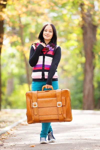Brunett tjej håller resväska på hösten alley i parken — Stockfoto