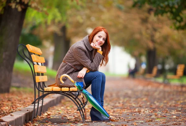Стильная рыжая девушка сидит на скамейке в осеннем парке . — стоковое фото