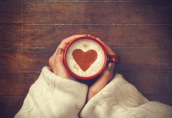 женщина держит горячую чашку кофе, с формой сердца
