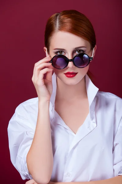 Pelirroja en gafas de sol sobre fondo rojo — Foto de Stock