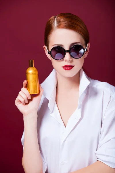 Ruiva em óculos de sol com perfume no fundo vermelho — Fotografia de Stock