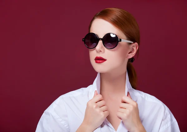 Rousse en lunettes de soleil sur fond rouge — Photo