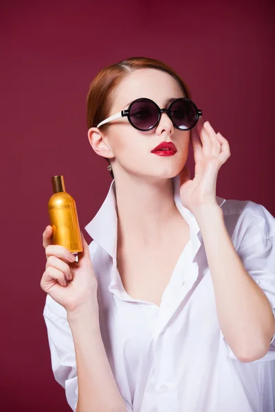 Ruiva em óculos de sol com perfume no fundo vermelho — Fotografia de Stock