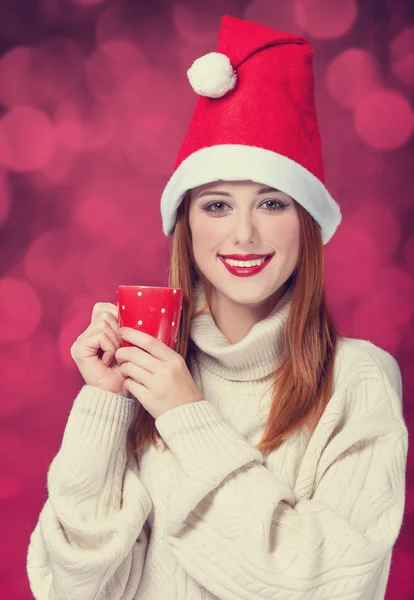 Рыжая девушка в рождественской шляпе с чашкой — стоковое фото