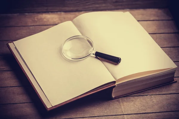 Loupa and book on wooden table — Stock Photo, Image