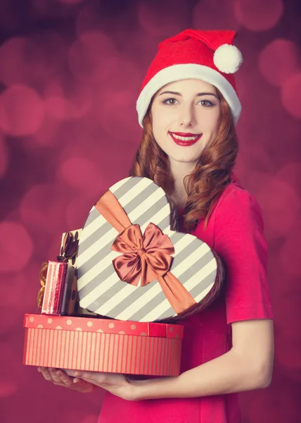 Rothaarige Mädchen mit Geschenken auf rotem Hintergrund — Stockfoto