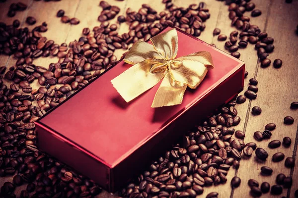 Presente vermelho na mesa de madeira com grão de café — Fotografia de Stock