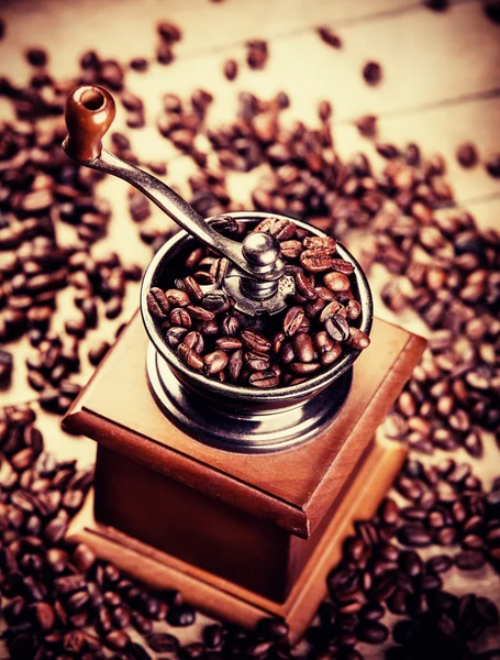 Młynek do kawy z ziaren kawy na drewnianym stołem — Zdjęcie stockowe