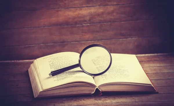 Loupa y libro sobre mesa de madera — Foto de Stock