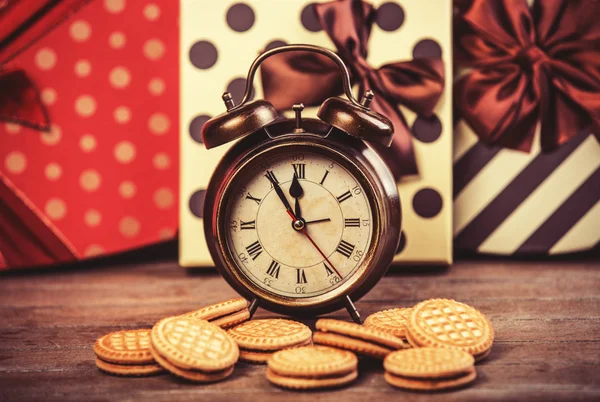 Relógio de alarme retro com biscoito em uma mesa . — Fotografia de Stock