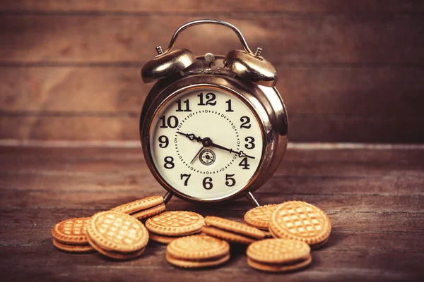Retro alarm clock with cookie on a table — Stock Photo, Image